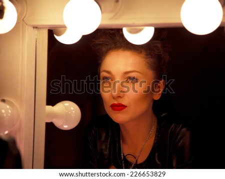 Young sassy woman with red lips in the dressing room in the dark before a mirror