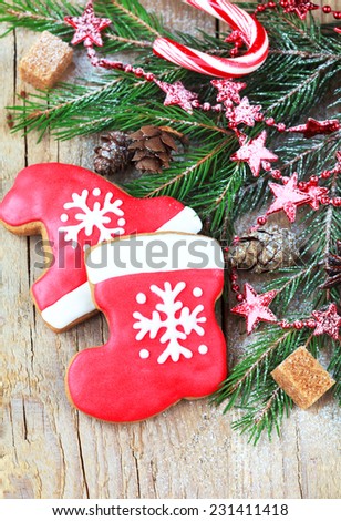 Homemade christmas gingerbreads painted as a red hat and boot of Santa with snowflake with with festive decoration on the wooden background with fir branches . Selective focus and place for text.