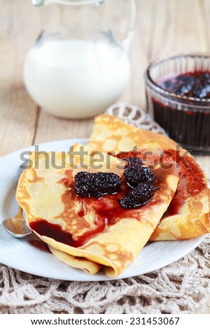 Pancakes with jam of black mulberry and small jam dish on a wooden table, selective focus