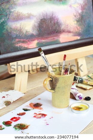 Workplace of the artist who paints a picture of the landscape using oily paints mounted on an easel. Selective focus on brush