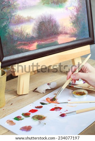 The artist paints a picture of the landscape using oily paints mounted on an easel. Selective focus on brush