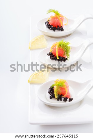 Appetizers in portion spoons of cream cheese, natural sturgeon black caviar, red salted salmon and dill on white table. Selective focus on the middle