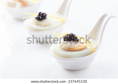 Appetizers in portion spoons of eggs, cream cheese, natural sturgeon caviar and lemon peel on a white background. Selective focus and space for text