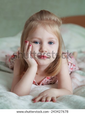 little blonde girl with painted nails lying on the bed