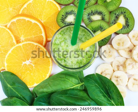 Healthy green smoothie with spinach, kiwi, bananas and oranges in a jar with green and yellow straws on a white table, selective focus