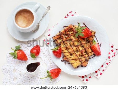 Belgium waffles with strawberries and chocolate decoration on plate with cup of coffee and small jar with chocolate on white table, selective focus