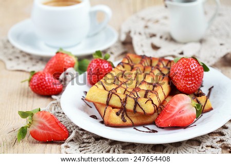 Belgium waffles with strawberries and chocolate decoration on plate with cup of coffee and small jar with chocolate on wooden table, selective focus