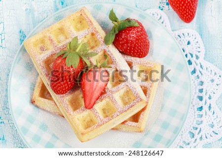 Homemade Belgium waffles with strawberries and powdered sugar on plate on blue table, selective focus
