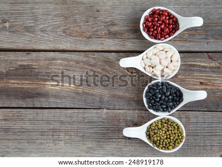 Set of different varieties of beans: baby lima, black small, adzuki and  mung in white ceramic spoons (appetizers) on wooden background, selective focus on beans