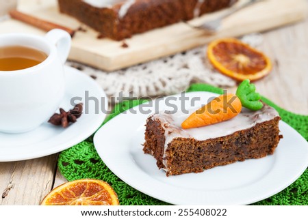 A piece of homemade carrot cake with nuts, decorated with marzipan carrots and cup of tea. Selective focus