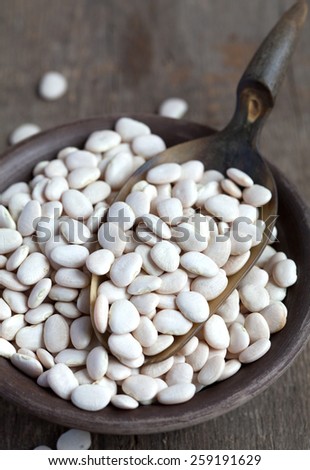 Dry white baby lima beans in a clay bowl on wooden table, selective focus