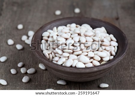 Dry white baby lima beans in a clay bowl on wooden table, selective focus