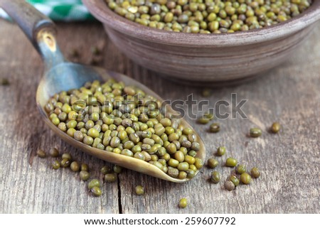 Dry green Mung beans in a clay bowl and in the scoop on wooden table, selective focus - some beans in focus, some are not