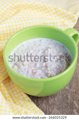 Green buckwheat porridge with milk on wooden table. Selective focus.