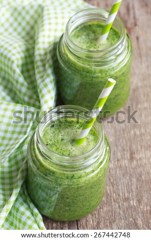 Healthy green smoothie made from spinach, kiwi, bananas and oranges in a jar with green straws on a wooden table, selective focus