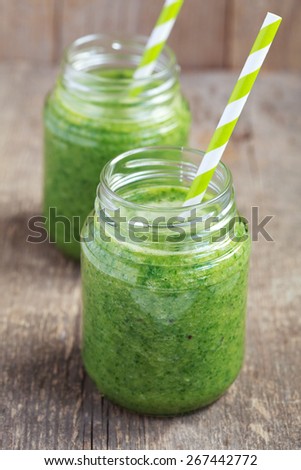 Healthy green smoothie made from spinach, kiwi, bananas and oranges in a jar with green straws on a wooden table, selective focus