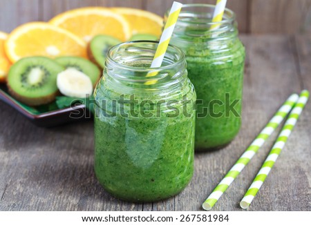 Healthy green smoothie made from spinach, kiwi, bananas and oranges in a jar with yellow straws on a wooden table, selective focus