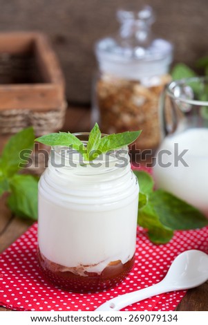 Breakfast: homemade yogurt with jam, granola and a jar with milk on a wooden table. Selective focus.