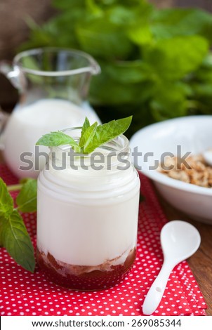 Breakfast: homemade granola in a white plate, yogurt with jam and a jug of milk on a wooden table. Selective focus.