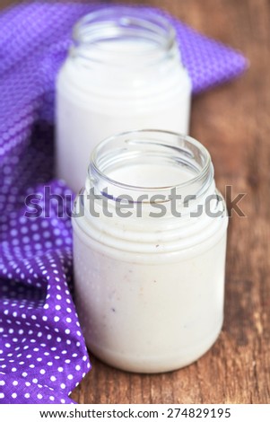Homemade yogurt with chopped prunes in two small glass jars on a wooden table with purple cloth, selective focus