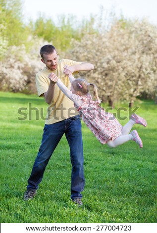 Dad playing with his baby daughter in a pink dress, he turns her around himself at arm\'s length, selective focus, the effect of motion