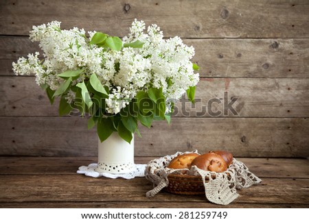 Still life. Bouquet of white lilacs in a vase and patties with apples on a wooden table. Rustic style and selective focus. Toned.