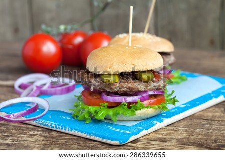 Homemade burgers with green salad, tomato, red onion, beef, pickled cucumbers and whole wheat bun on a wooden table, selective focus