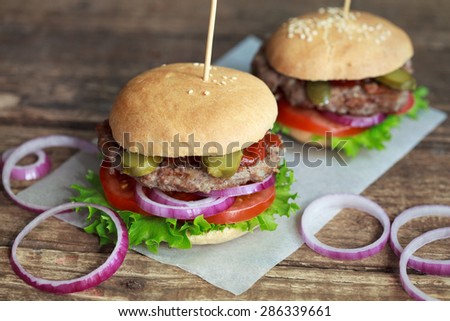 Homemade burgers with green salad, tomato, red onion, beef, pickled cucumbers and whole wheat bun on a wooden table, selective focus
