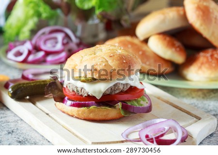 Homemade burgers with green salad, tomato, red onion, beef, pickled cucumbers, mozzarella cheese and  buns with sesame seedson a wooden table, selective focus