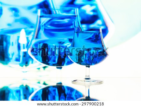 Art. Blue cocktail in the glass with ice cubes on a color background with reflections behind, abstract background