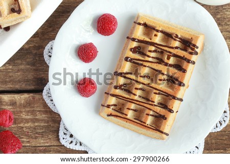 Belgium whole wheat waffles with raspberries and chocolate decoration on plate on wooden table, selective focus