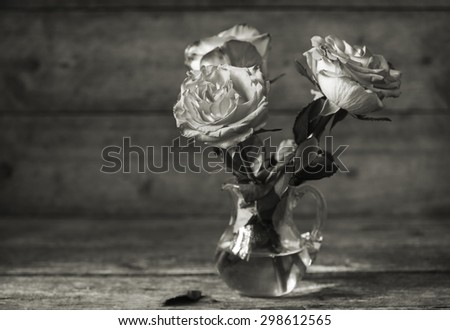 Still life: black and white roses in a glass jug on a old wooden table. Selective focus
