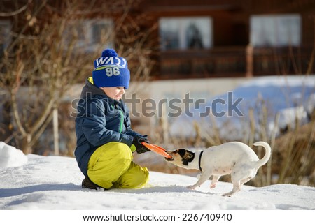 A little boy is playing with a dog on the snow outside