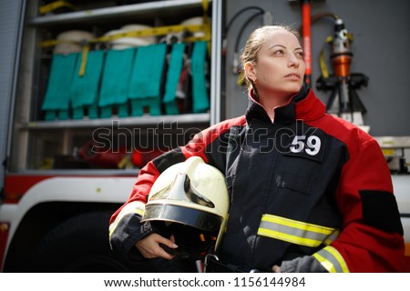 Photo of young woman firefighter looking to side next to fire engine