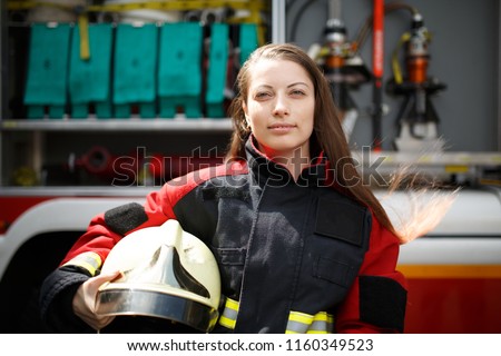 Photo of young firefighter woman staring into camera with long hair next to fire engine