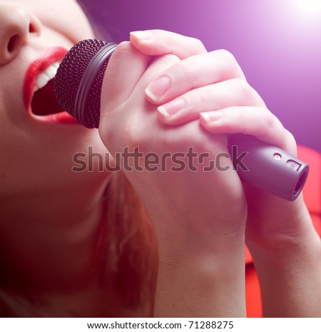 Woman sing over color background. Focused on microphone