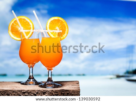Two bocals of Tequila Sunrise cocktails on a beach table near ocen. Have a little break