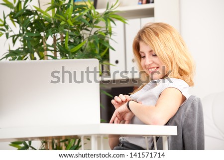 smiling woman sitting and looking at her watch in the office