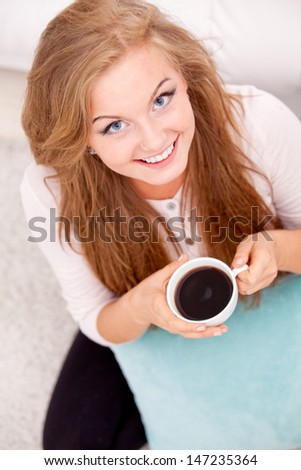 Overhead view of woman sitting on floor with some coffee and pillow at home