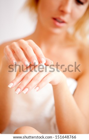 Young woman applies cream on hands over white, focus on hands