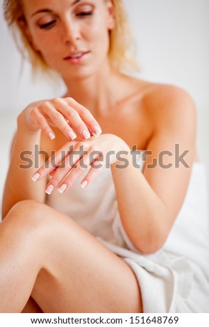 Young woman applies cream on hands over white, focus on hands