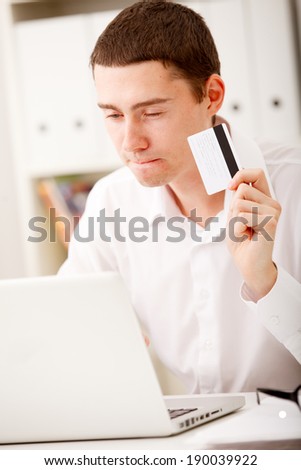 Handsome man holding credit card and using laptop