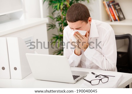 man sneezing while working in office