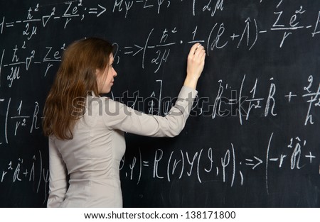 A student girl writing formulas on school blackboard