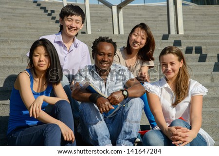 Multiethnic group of five university students sitting on steps of university smiling, metaphor for diversity and international friendship