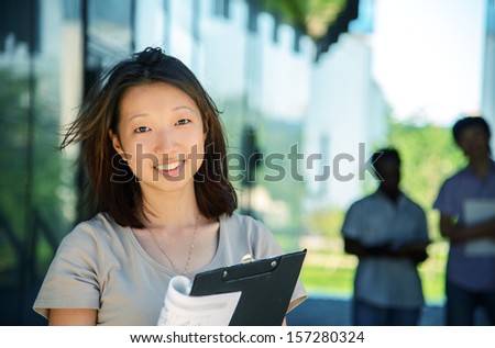 Portrait Of Smiling Asian University Student Girl Standing Outside With Several Other Students On Background