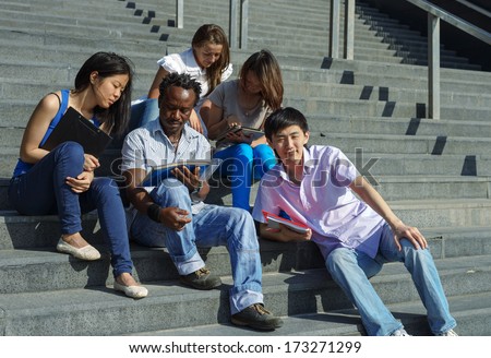 Multiethnic group of five university students sitting on steps of university smiling