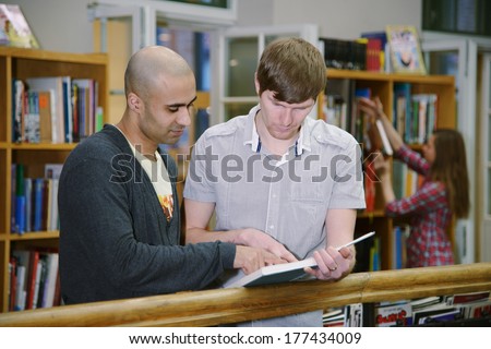 Portrait of two students, european and middle eastern, standing with books in university library