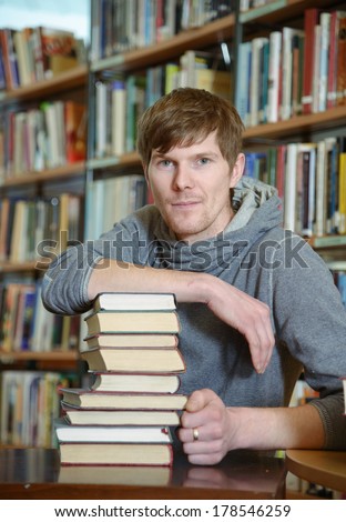 Portrait of male student sitting at desk in Begen city library with a pile of books and looking at camera