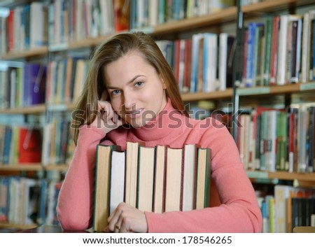 Portrait of beautiful student girl sitting at desk in Begen city library with a pile of books and looking at camera